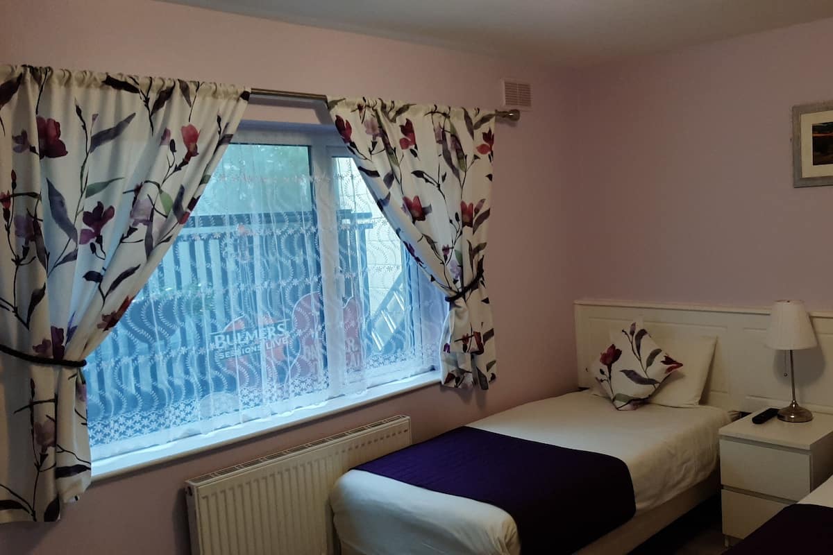 A bedroom with a window, a bed, a bedside table, and a nightstand.