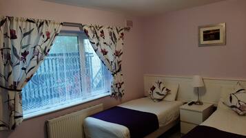 A bedroom with a window, a bed, a bedside table, and a nightstand.