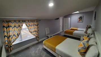 Quarto de hotel com duas camas, uma janela com cortinas em padrão Chevron, um radiador, uma cadeira e um quadro na parede.