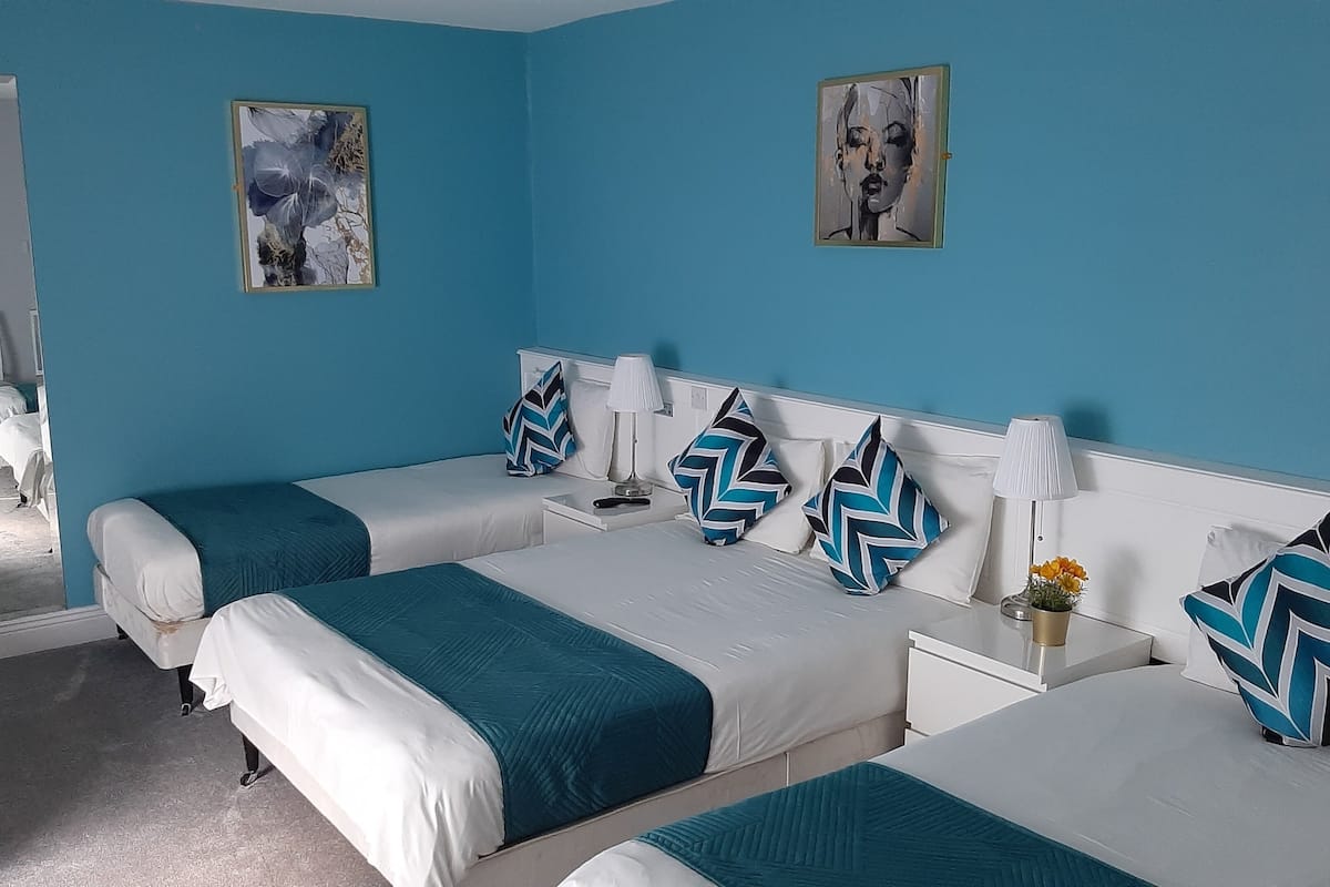 A hotel room with two beds, a white headboard, and a blue wall. There are two paintings on the wall, a lamp on each nightstand, and a vase with flowers on the right nightstand.