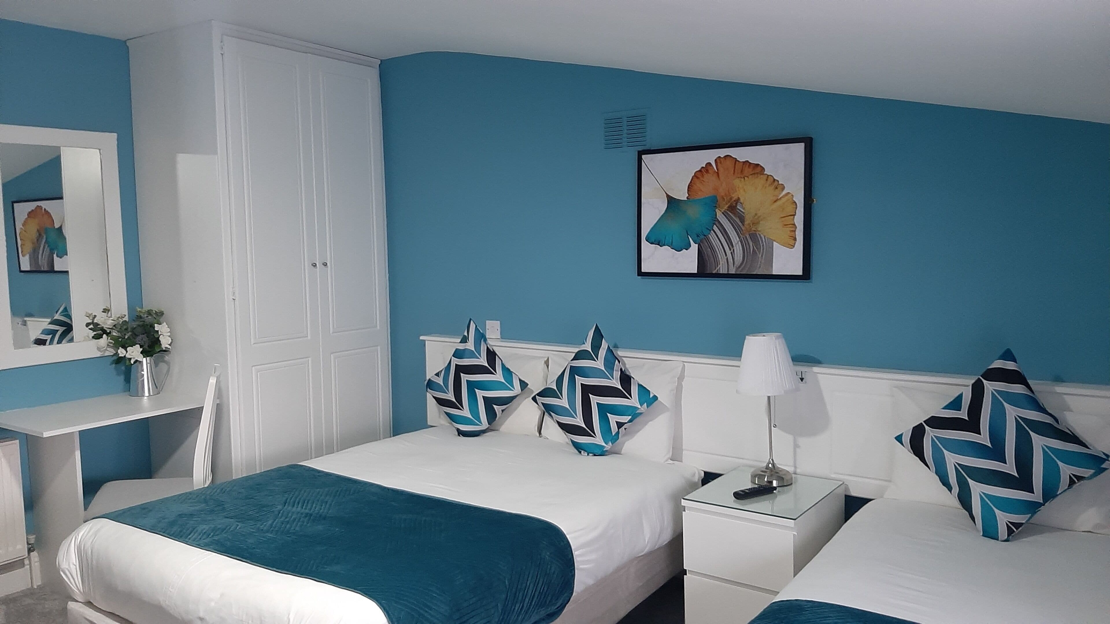 A bedroom with two beds, a nightstand, a bedside table, a mirror, a wall-mounted picture, and a window.