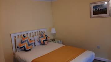 A neatly made bed with a white headboard, two decorative pillows, a bedside lamp, and a framed picture on the wall.