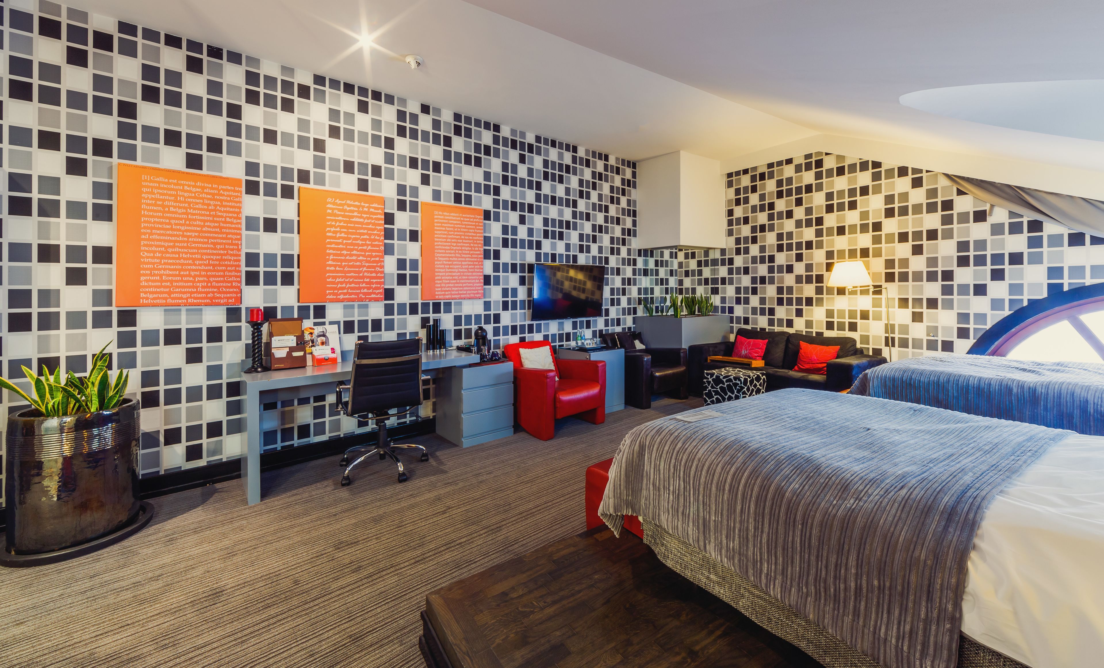 A modern hotel room with a check-in desk, a flat-screen TV, a sofa, a bed, and a patterned wall.