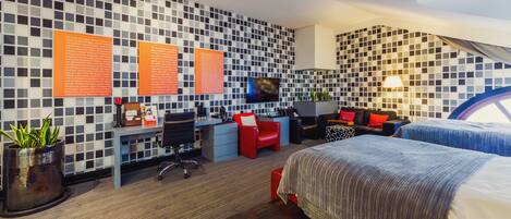 A modern hotel room with a check-in desk, a flat-screen TV, a sofa, a bed, and a patterned wall.