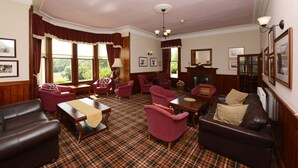 A traditional room with a fireplace, plaid carpet, and classic furniture including leather sofas and armchairs. - The Inch Hotel (Fort Augustus)