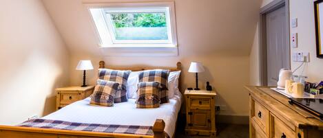 A bedroom with a bed, two nightstands, a wooden dresser, a skylight, and a view of greenery outside.