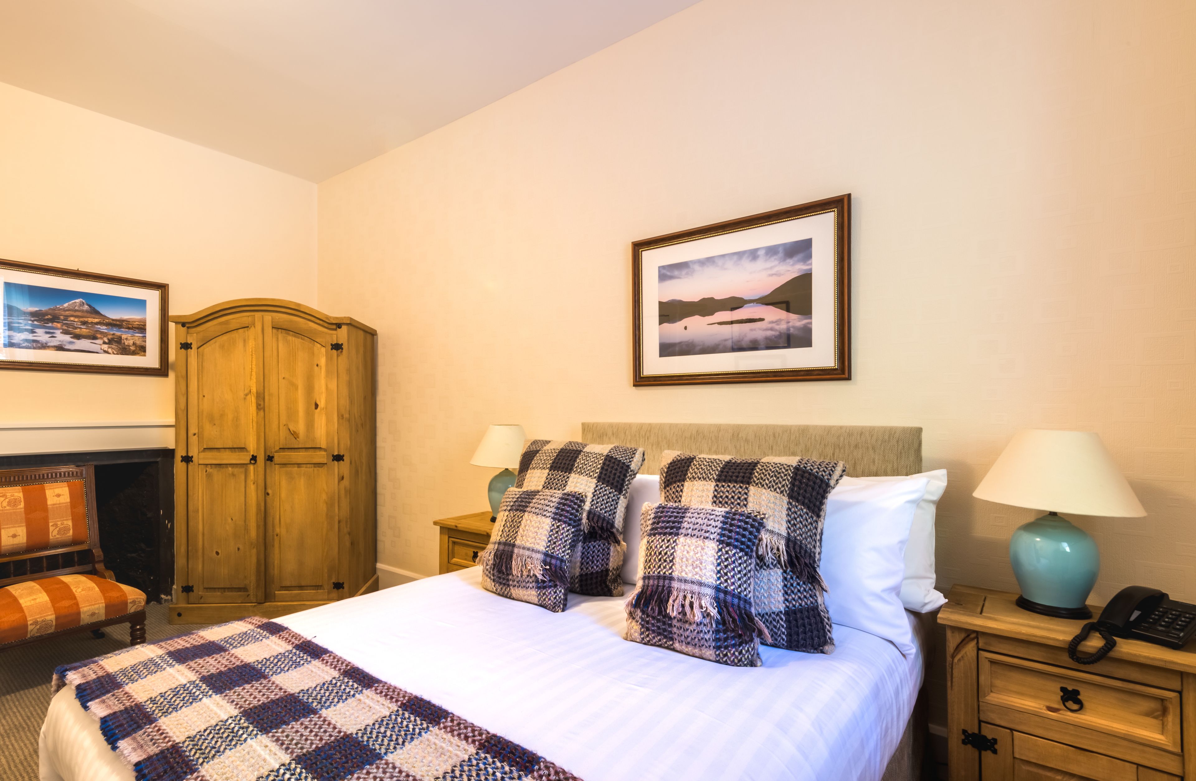 Una habitación de hotel con cama, dos mesitas de noche, un armario de madera, un banco y una chimenea.