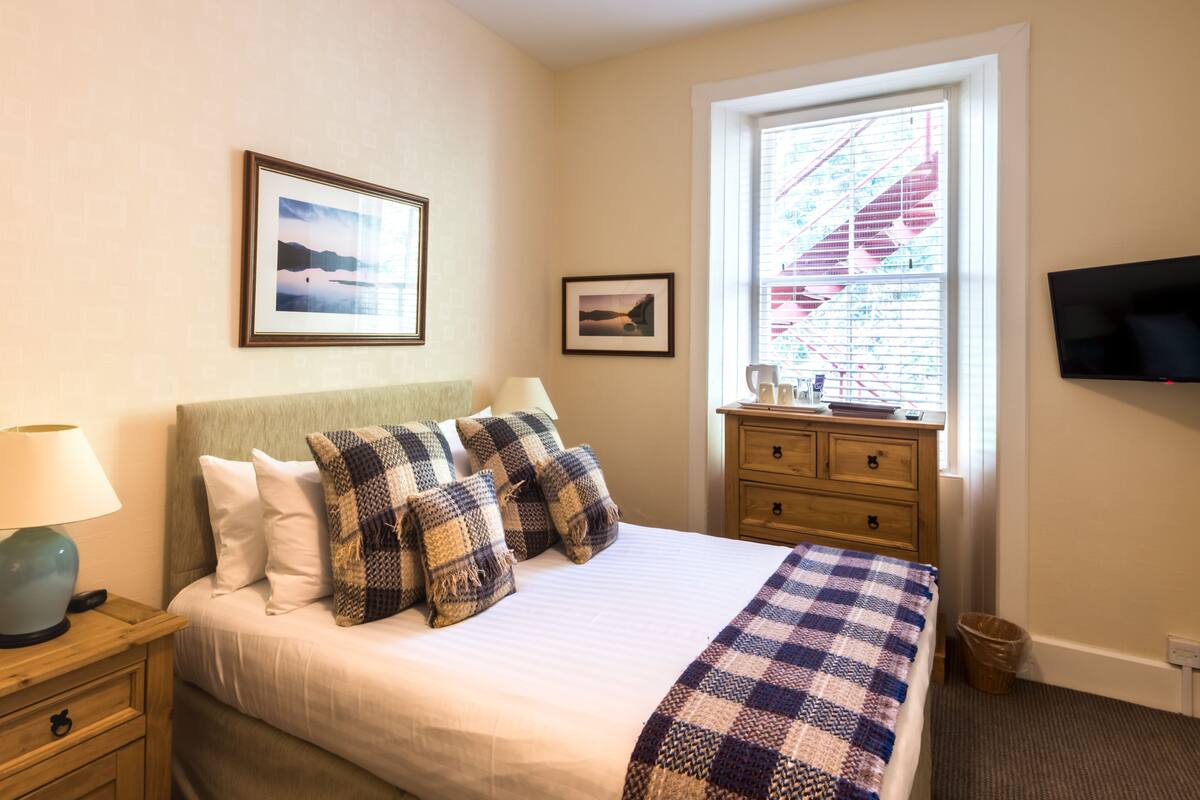 A neatly made bed with a checkered blanket, a bedside lamp, and a framed picture on the wall.