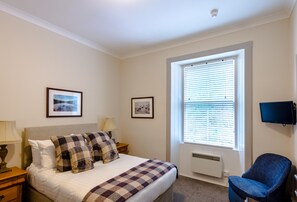 A hotel room with a bed, a chair, a television, and a window with blinds.
