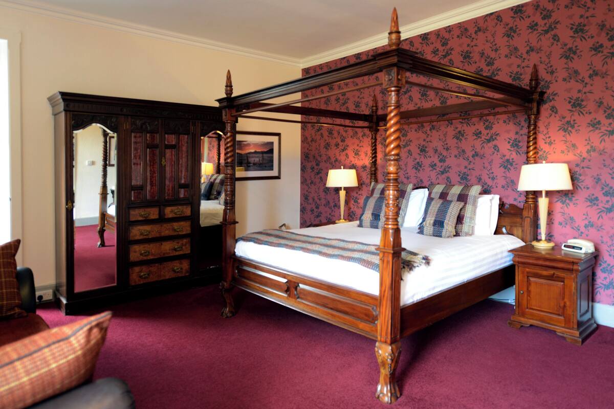 A four-poster bed with a wooden frame, a nightstand with a lamp, and a dresser with drawers.