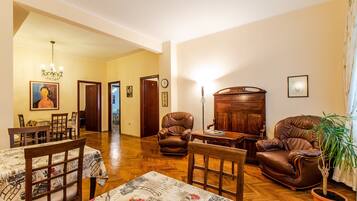 A spacious living room with a wooden floor, a dining area with a table and chairs, and a large brown leather armchair.