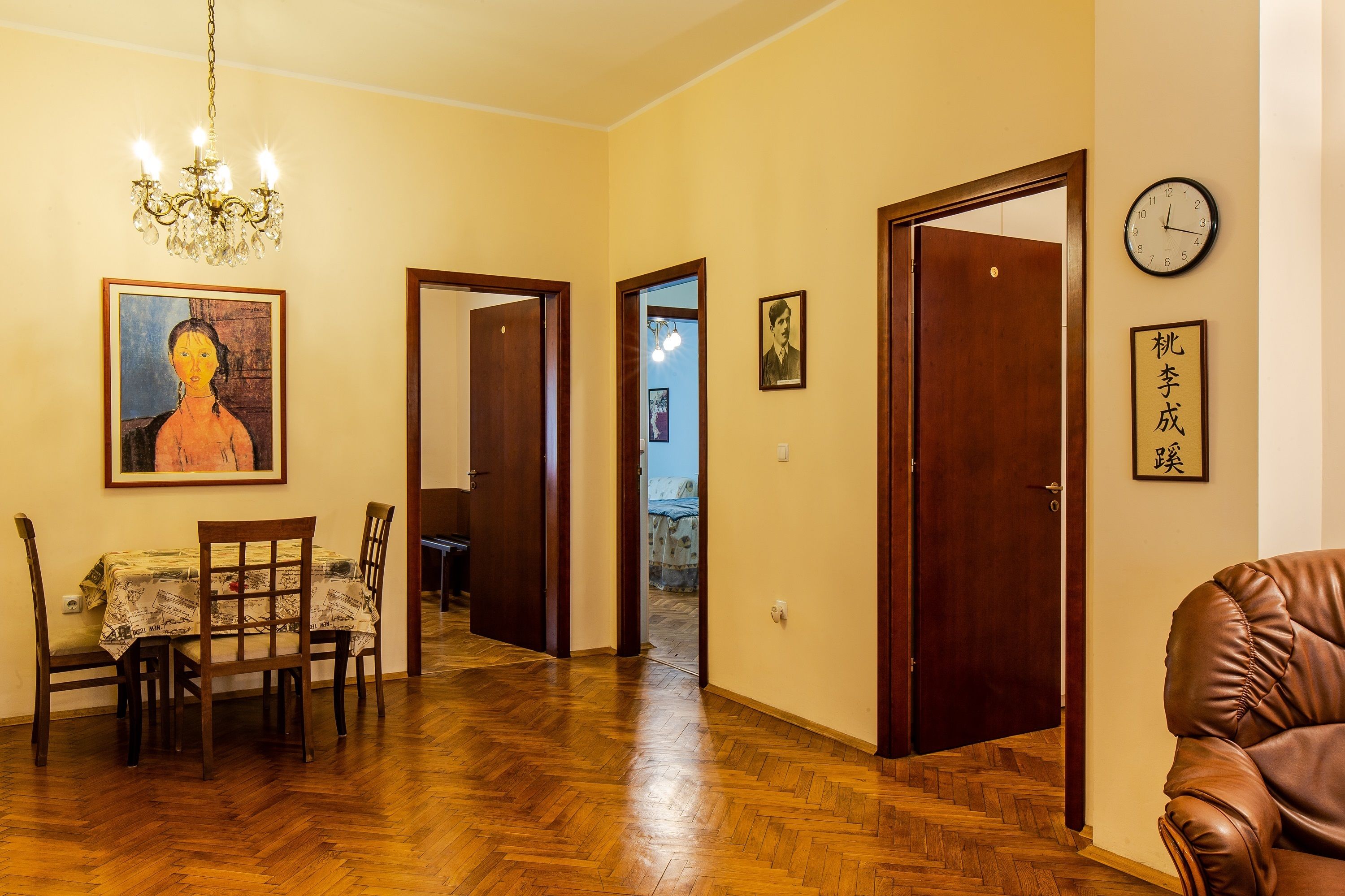 Una stanza con pavimento in legno, un tavolo da pranzo con sedie, un lampadario e un orologio appeso al muro.