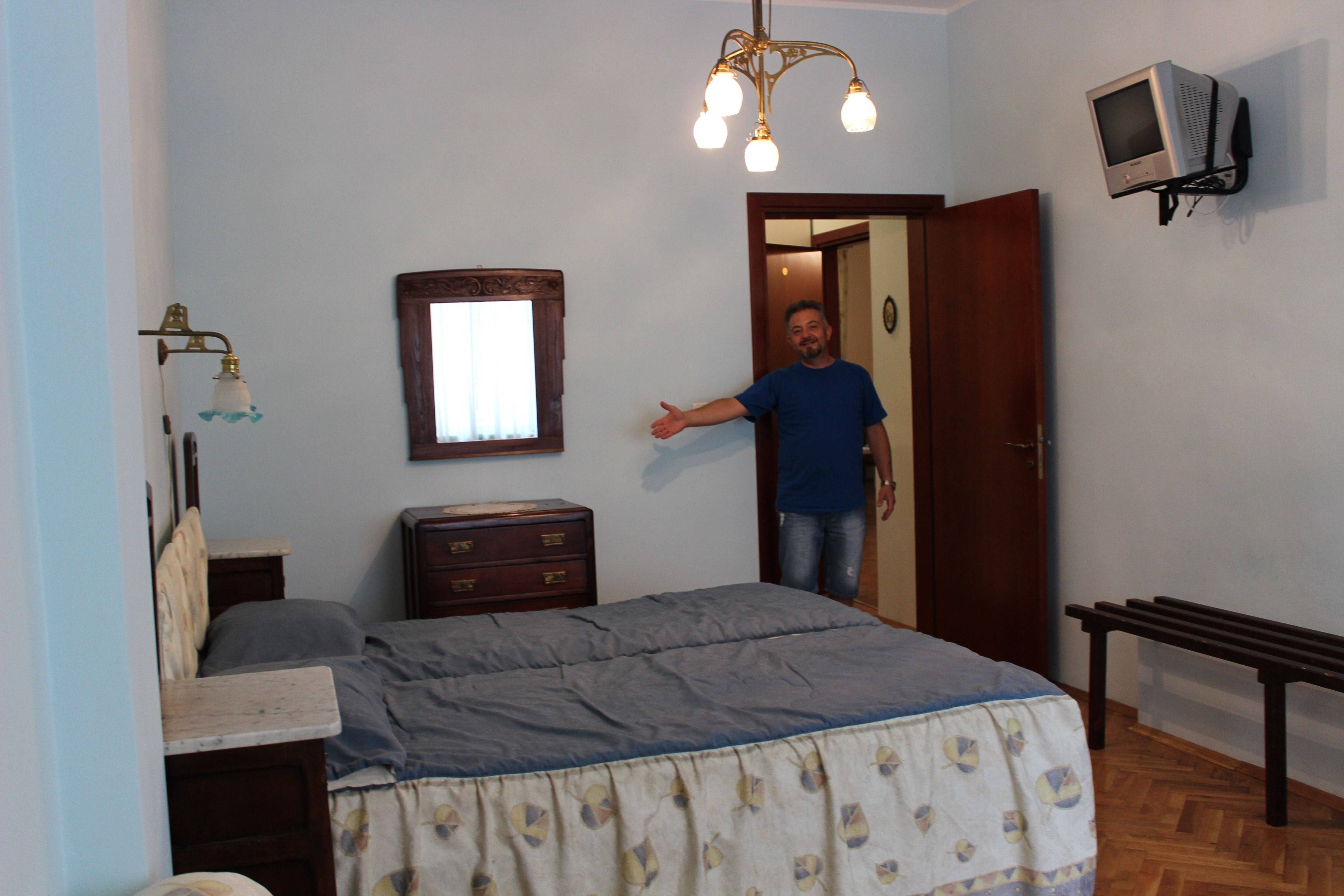 Un dormitorio con cama, cómoda, espejo y televisor montado en la pared.