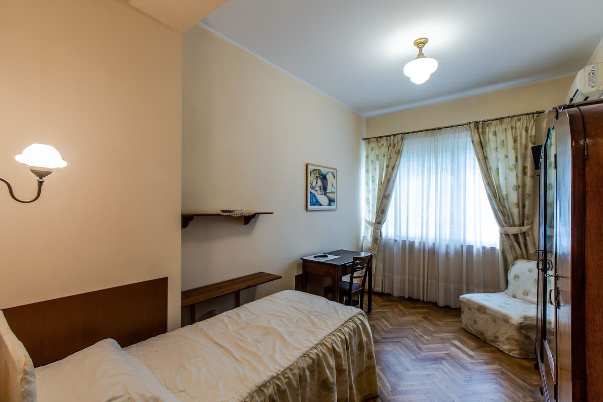 A bedroom with a bed, a desk, a chair, a wardrobe, and a window with curtains.