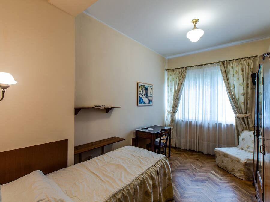 Une chambre à coucher comprenant un lit, un bureau, une chaise, une armoire et une fenêtre avec des rideaux.
