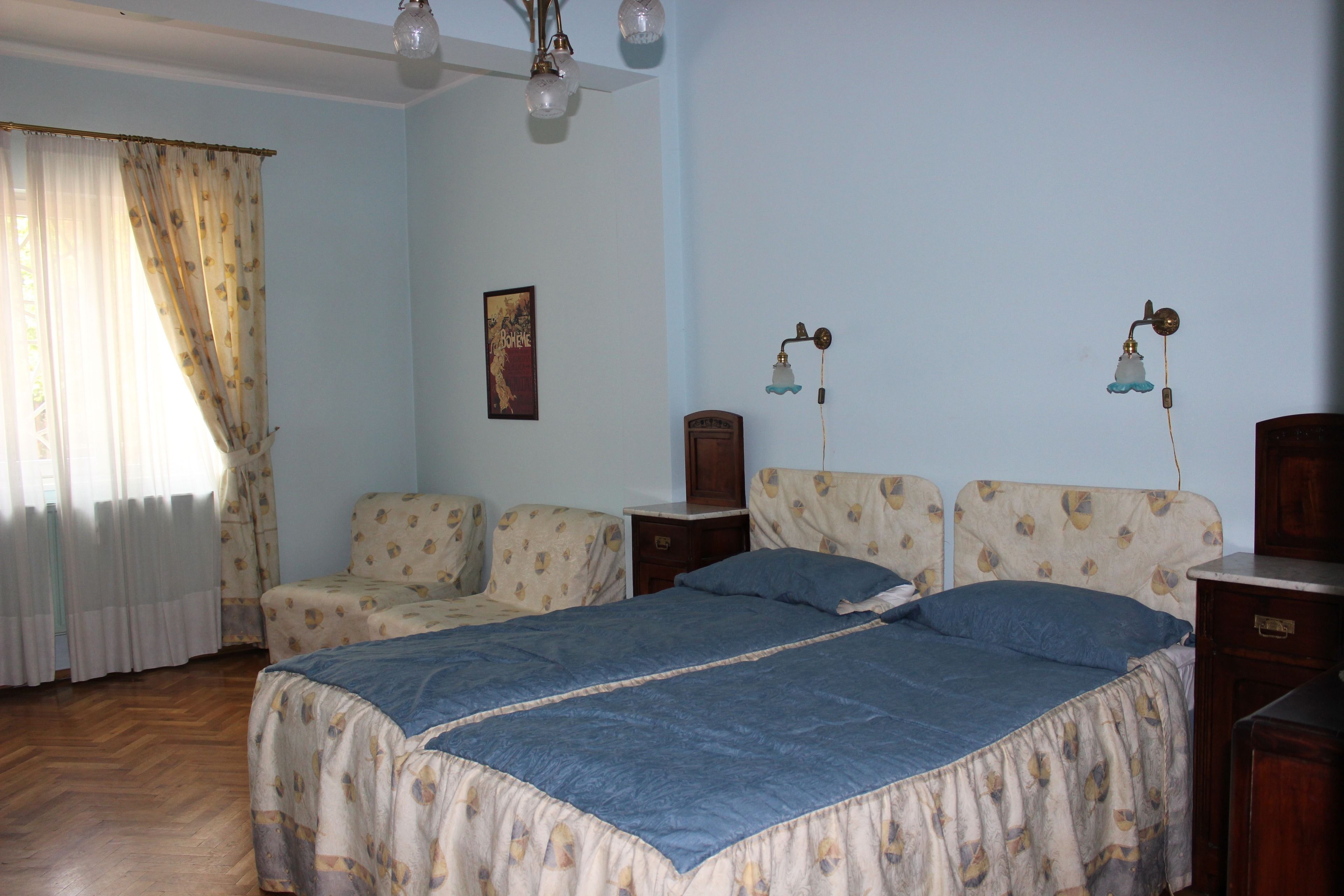 Un dormitorio con una cama, dos mesitas de noche, una lámpara y una ventana con cortinas.