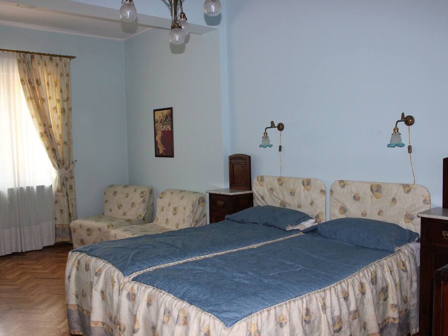 Un dormitorio con una cama, dos mesitas de noche, una lámpara y una ventana con cortinas.