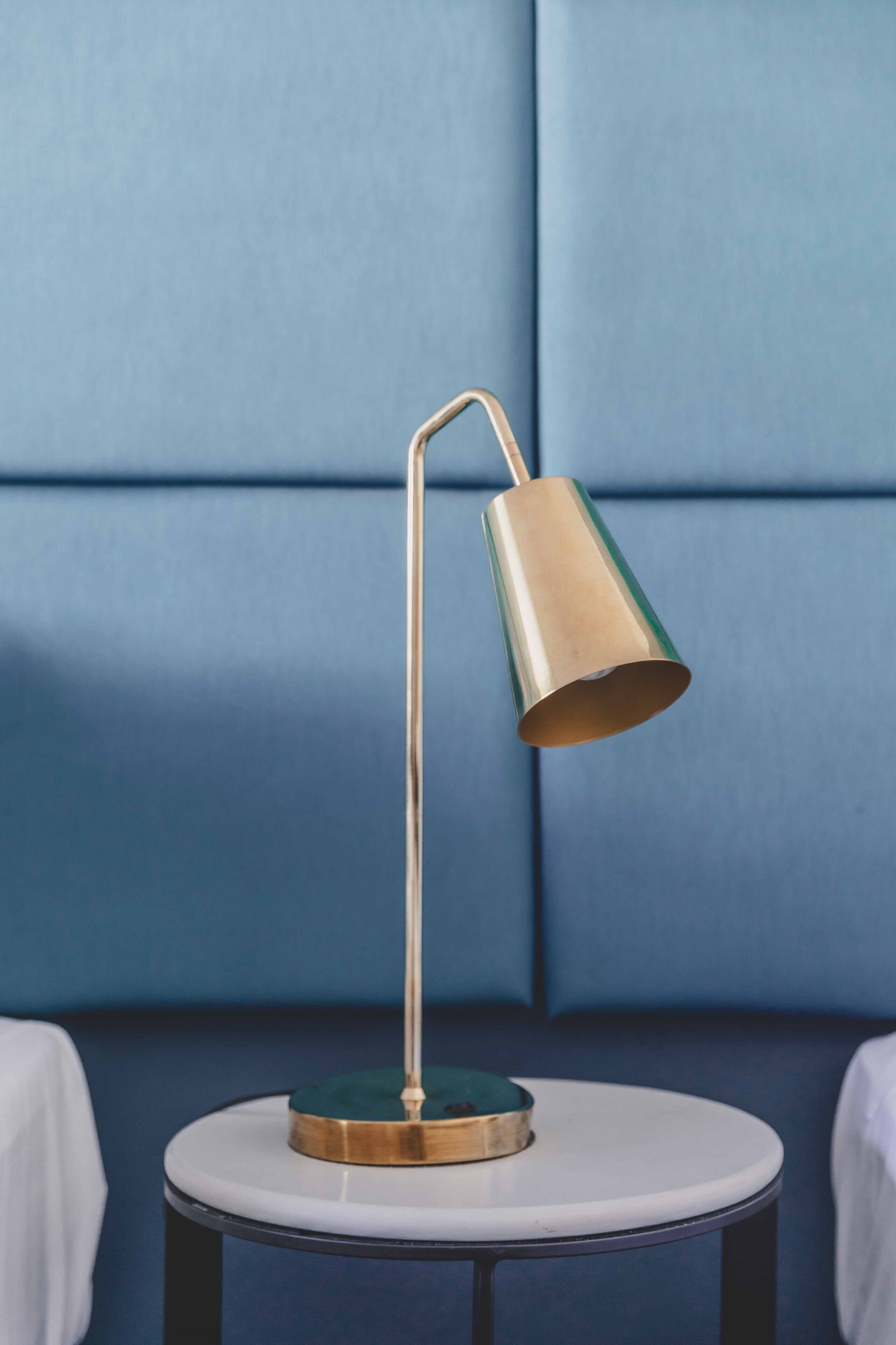 Una mesa redonda con una lámpara de pie metálica frente a una pared azul.