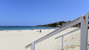 A beach with a staircase leading down to the sand, a clear blue sky, and buildings in the background. - Avoca Randwick by Sydney Lodges (Randwick)