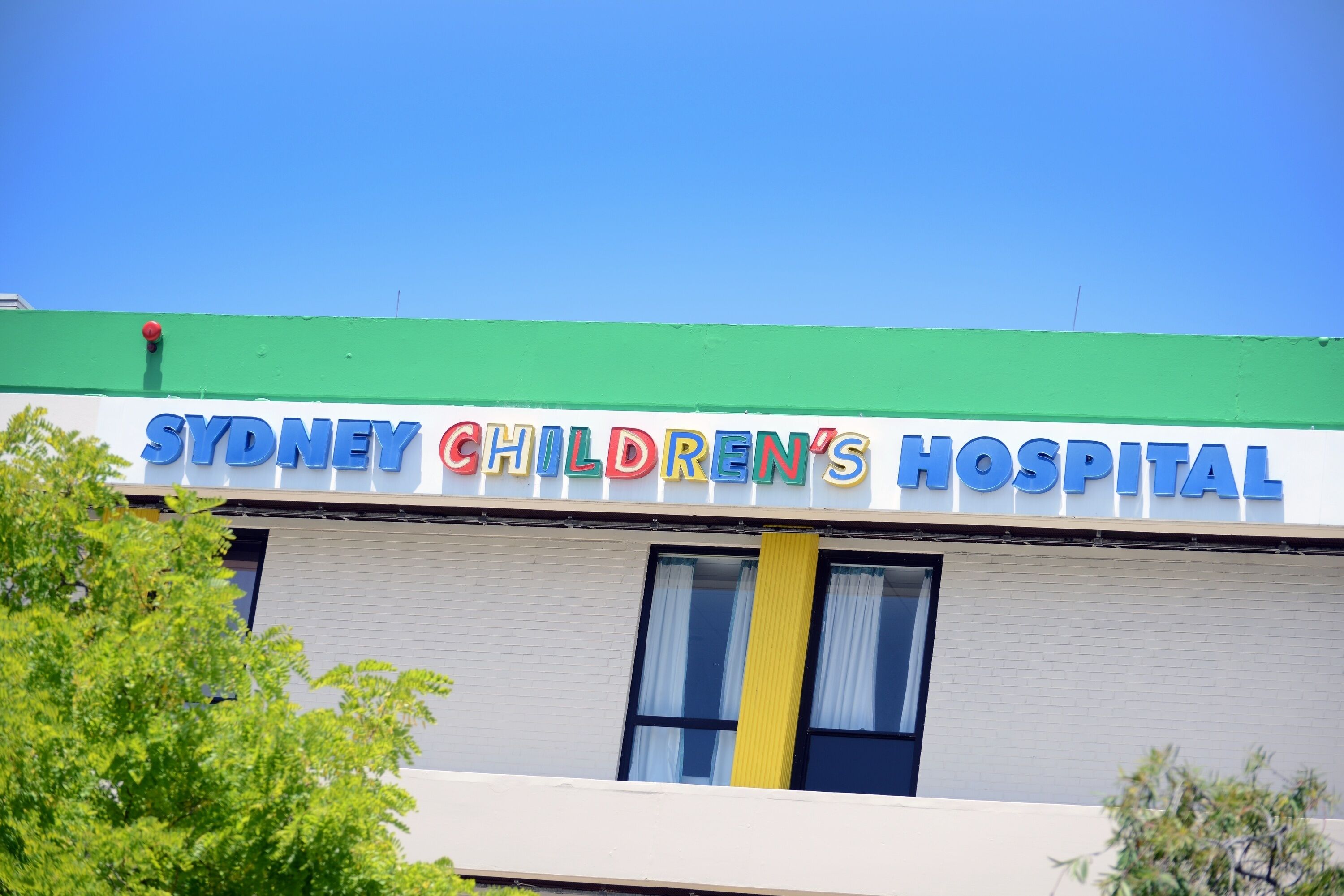 Exterior del Hospital Infantil de Sydney, con techo verde y cielo azul despejado.