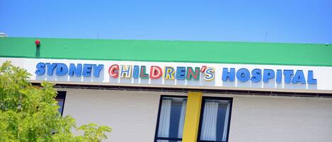 Exterior del Hospital Infantil de Sydney, con techo verde y cielo azul despejado.