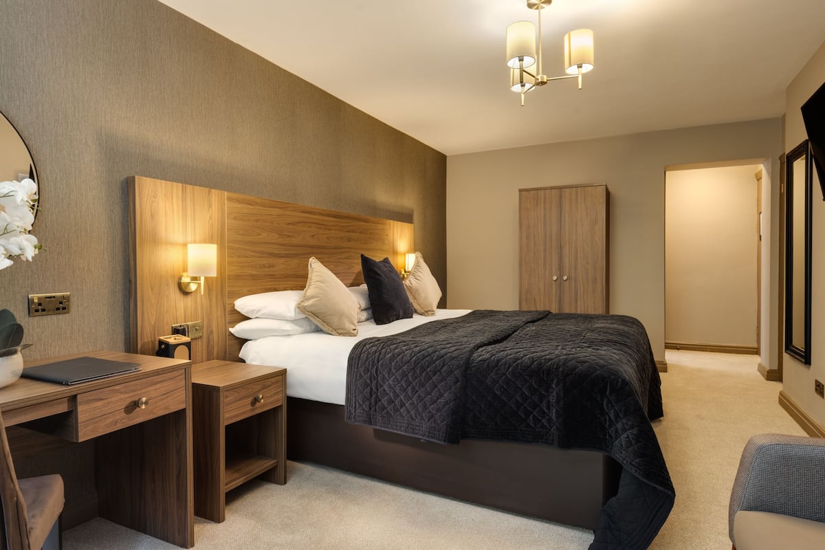 A modern hotel room with a large bed, bedside tables, a desk, and a wardrobe.