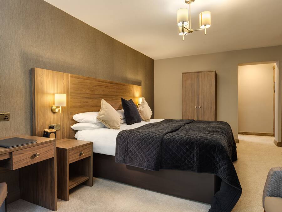 A modern hotel room with a large bed, bedside tables, a desk, and a wardrobe.