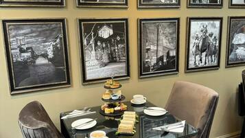 Un comedor con mesa de vidrio, fotografías en blanco y negro en la pared, y una selección de sándwiches y pasteles.