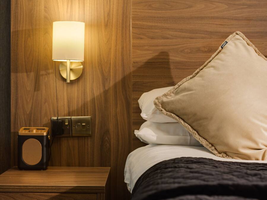 A neatly made bed with a black comforter and a beige pillow, a bedside table with a lamp, and a small radio.