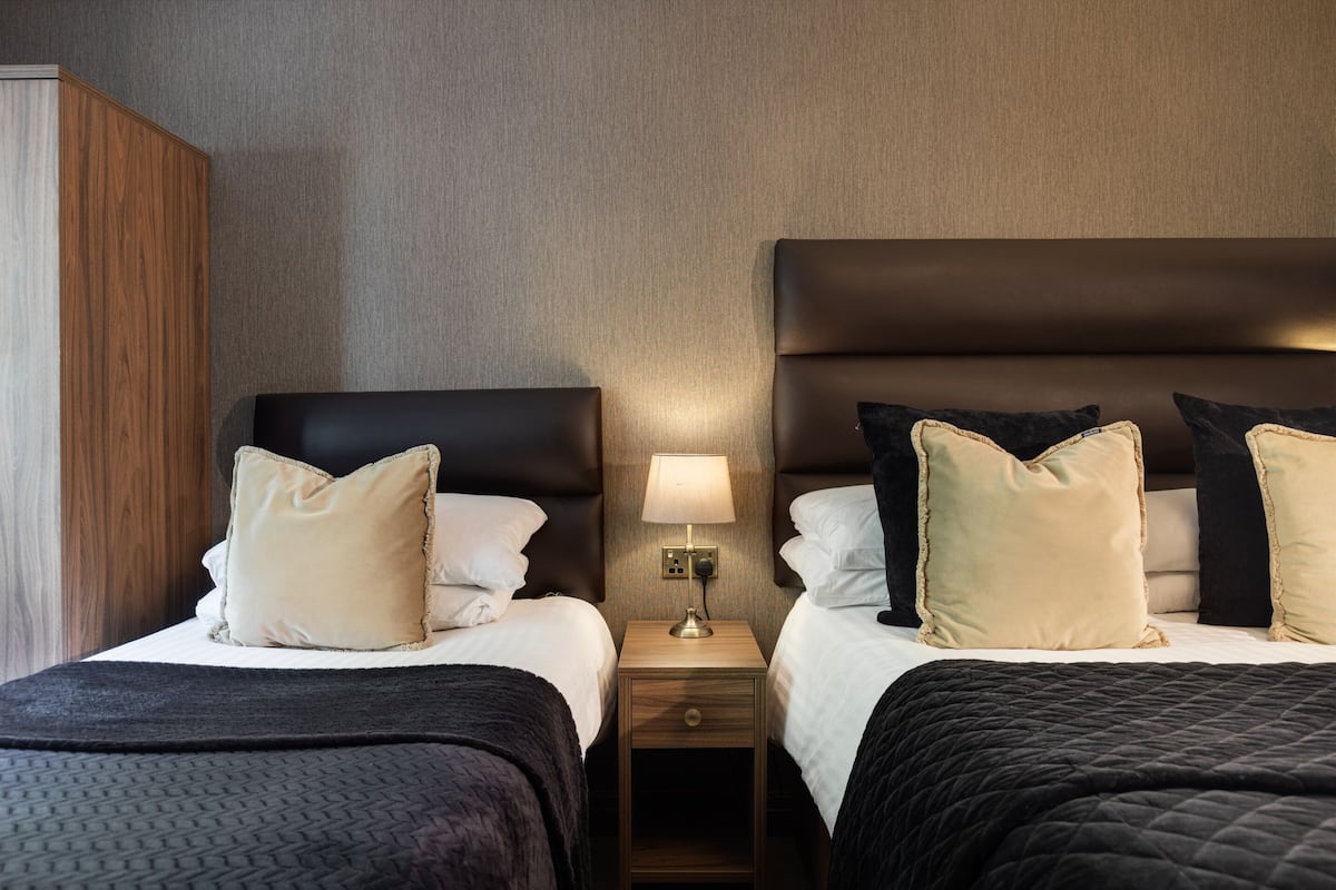 A hotel room with two beds, each with a headboard, a nightstand with a lamp, and a wardrobe.