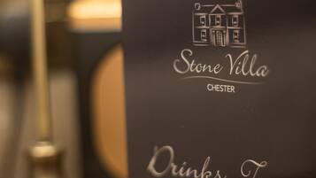 Ein schwarzes Schild mit der Aufschrift "Stone Villa Chester" und "Getränke, Leckereien & Geschenke" auf einer Holzoberfläche.