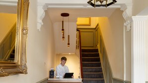 Un área de recepción con piso a cuadros, un mostrador, una silla, un espejo grande y una escalera.