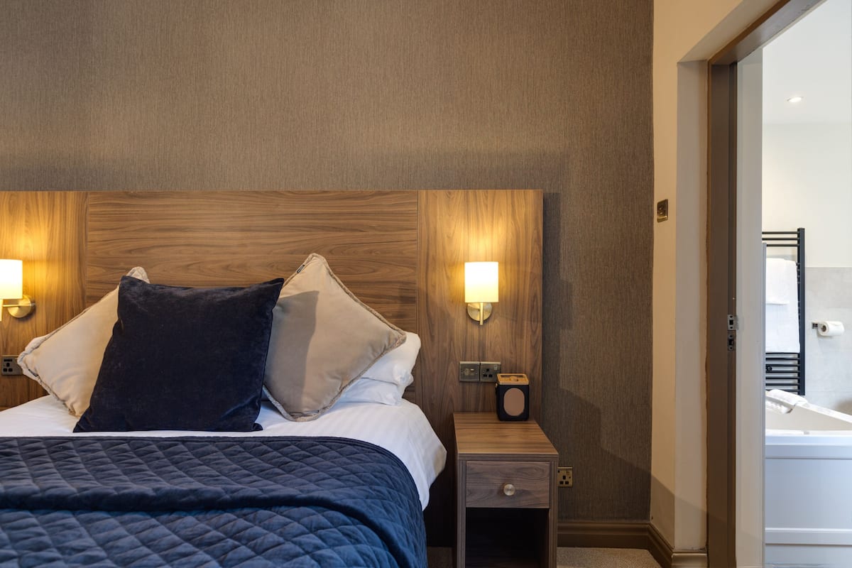 A hotel room with a large bed, two bedside lamps, a nightstand with a radio, and a view of a bathroom.