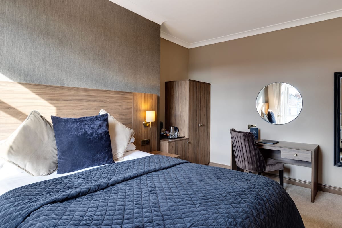 A hotel room with a large bed, a desk, a wardrobe, and a round mirror.