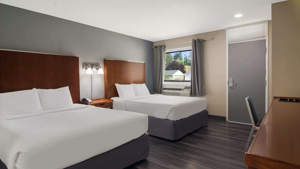 A hotel room with two beds, a desk, and a window with curtains.