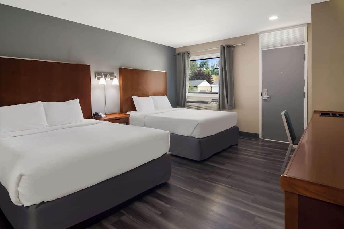 A hotel room with two beds, a desk, and a window with curtains.