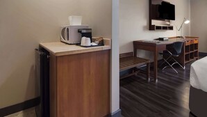 A hotel room with a wooden desk, a chair, a bed, a TV mounted on the wall, and a coffee maker on the desk.