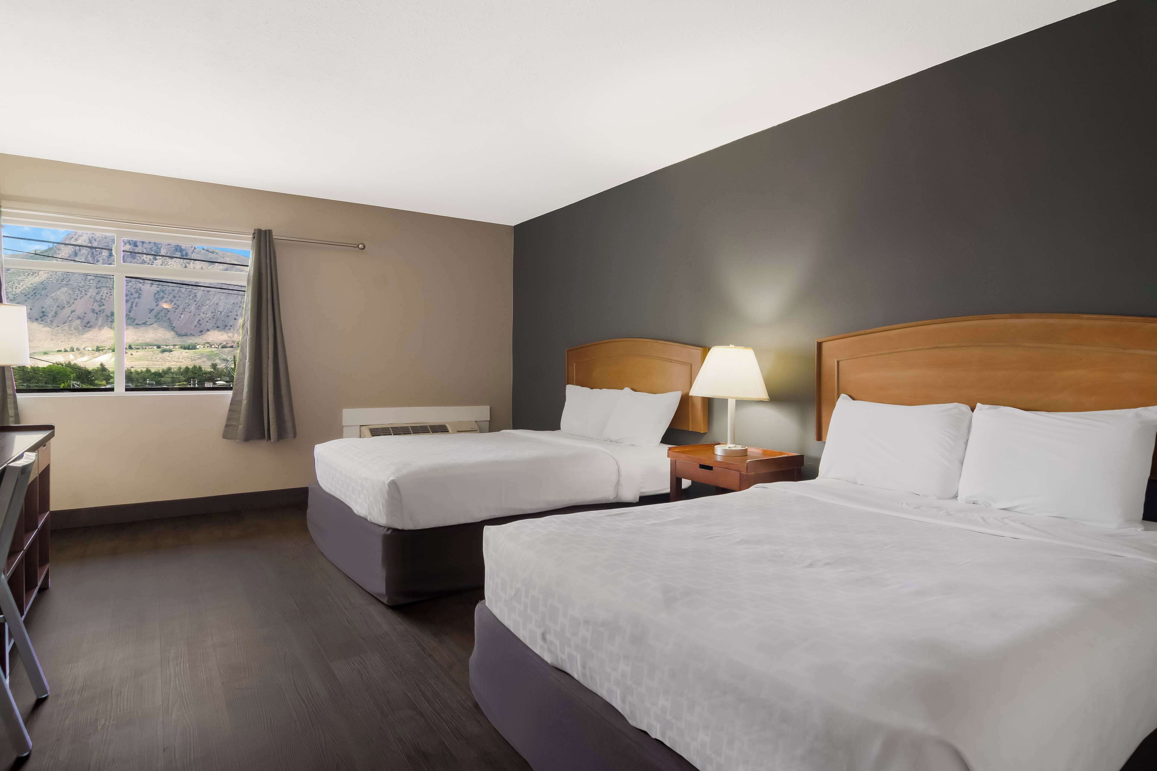 Quarto de hotel com duas camas, uma escrivaninha e janela com vista para as montanhas.