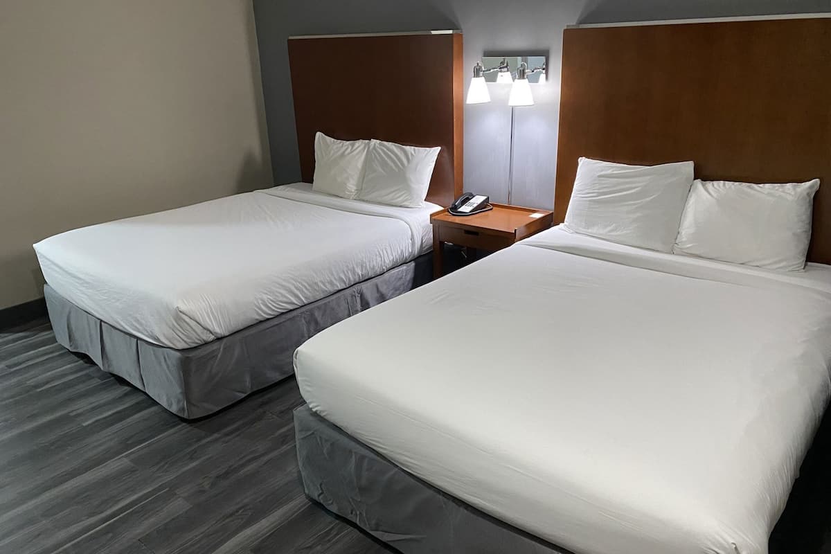Two adjacent beds with wooden headboards, a nightstand with a telephone, and a wall-mounted light fixture.