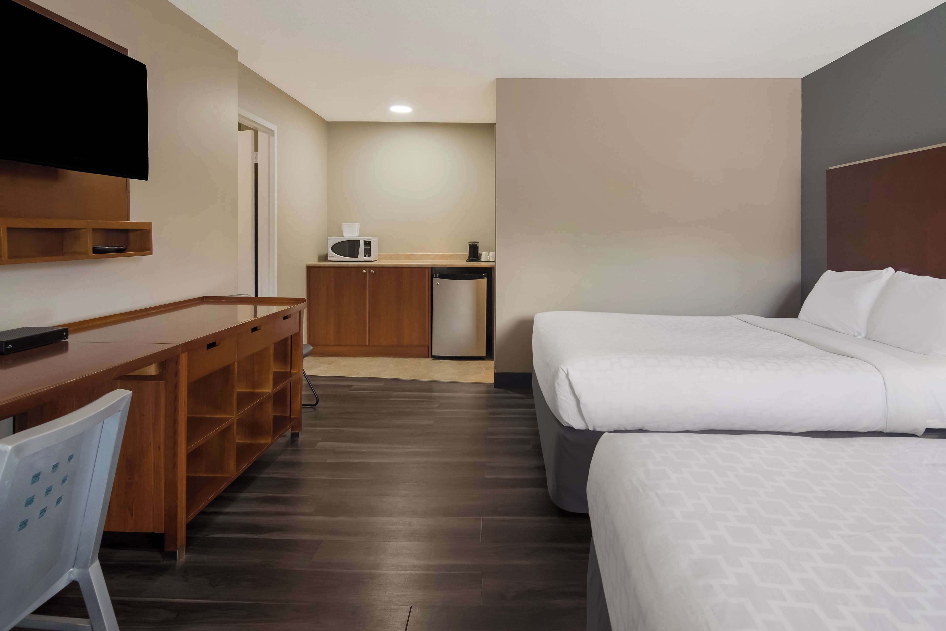 Habitación de hotel con cama, escritorio, silla, televisión, microondas y pequeña cocina.