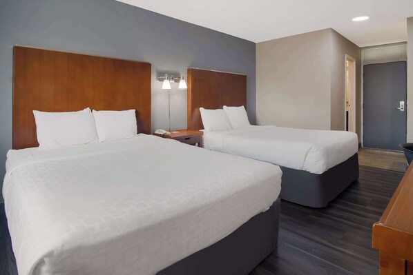 Habitación de hotel con dos camas, un cabecero de madera, una mesita de noche con lámpara y una puerta a la derecha.