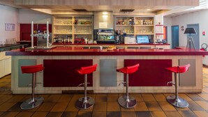 A bar area with a red counter, multiple shelves with bottles, a coffee machine, and three red bar stools. - Logis Hôtel Noemys Brive - Restaurant Le Teinchurier (Brive-la-Gaillarde)