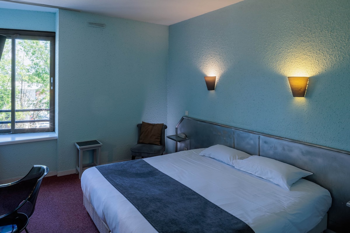 Habitación de hotel con cama, una silla, mesita de noche y dos lámparas de pared.