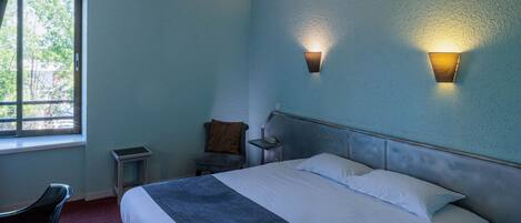 A hotel room with a bed, a chair, a nightstand, and two wall-mounted lights.