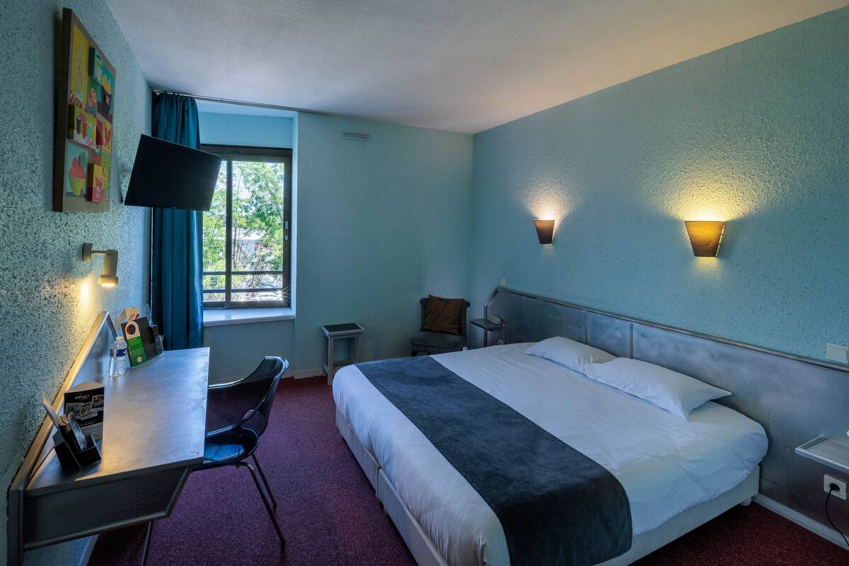 Una habitación de hotel con cama, escritorio, silla y televisor en la pared.