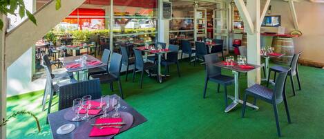 An outdoor dining area with tables set for two, featuring green carpeting and black chairs.