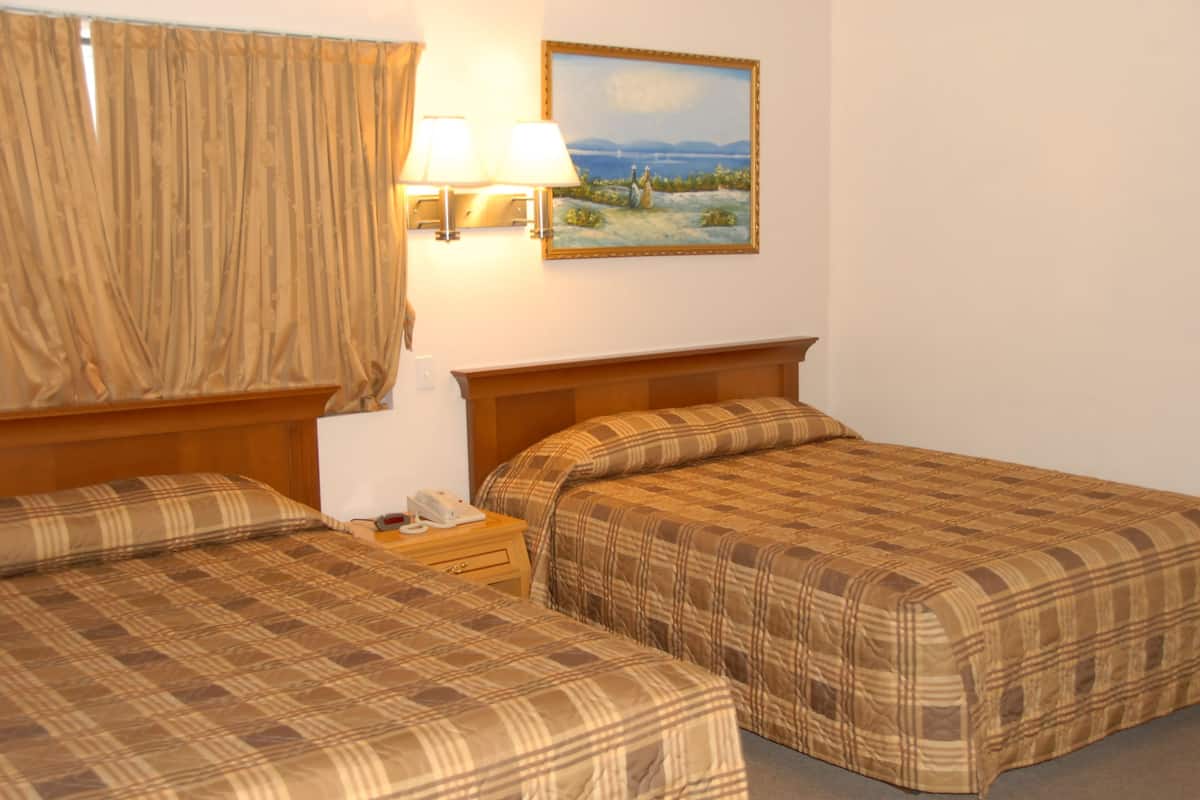 A hotel room with two beds, a nightstand, a lamp, and a painting on the wall.