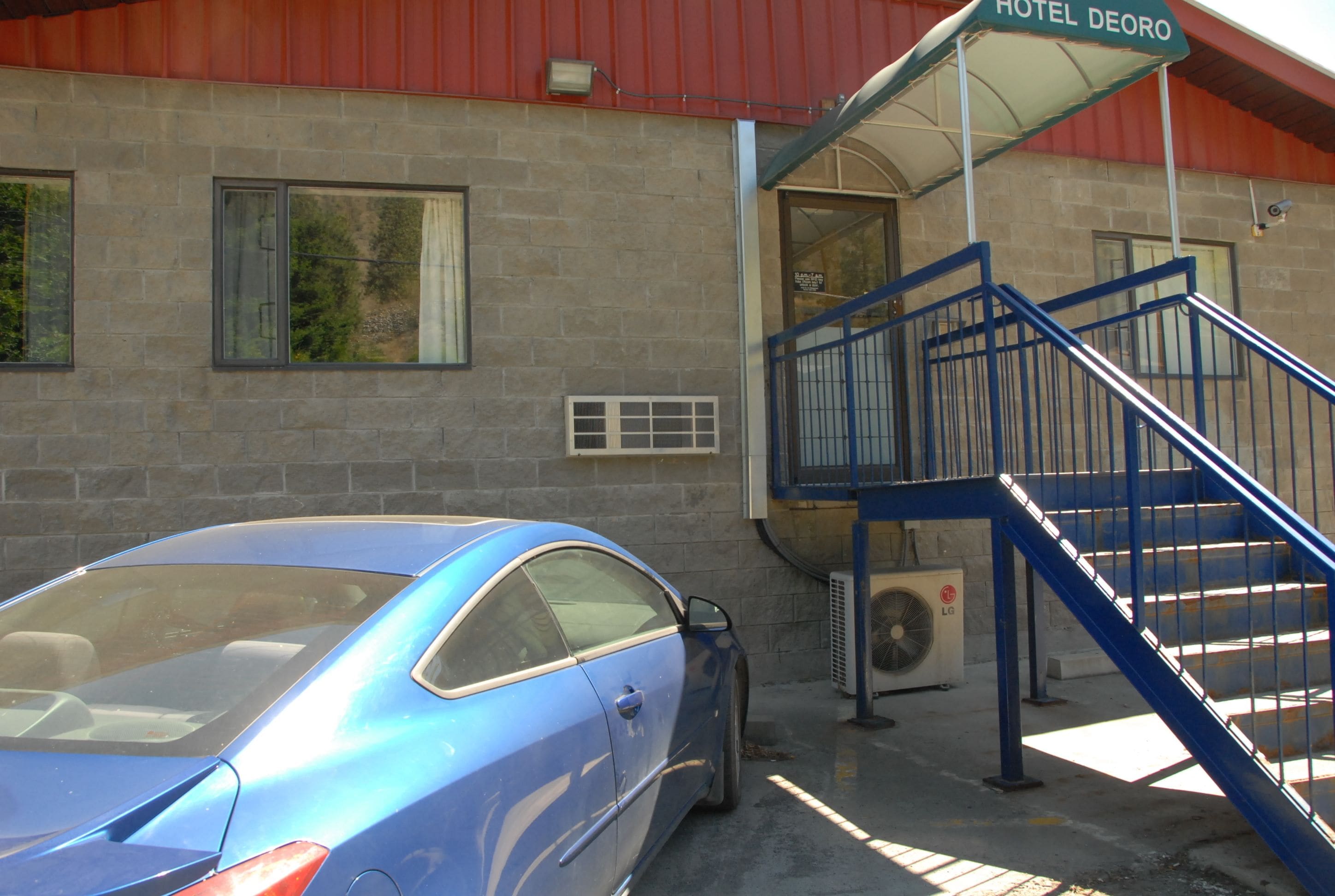 A blue car parked in front of a building with a sign reading "HOTEL DEORO".