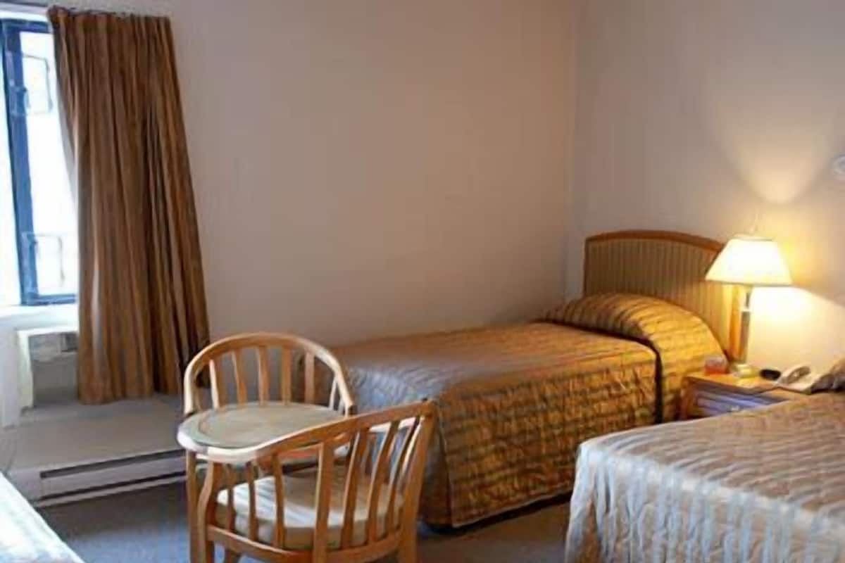 A hotel room with two beds, a chair, a lamp, and a window with curtains.