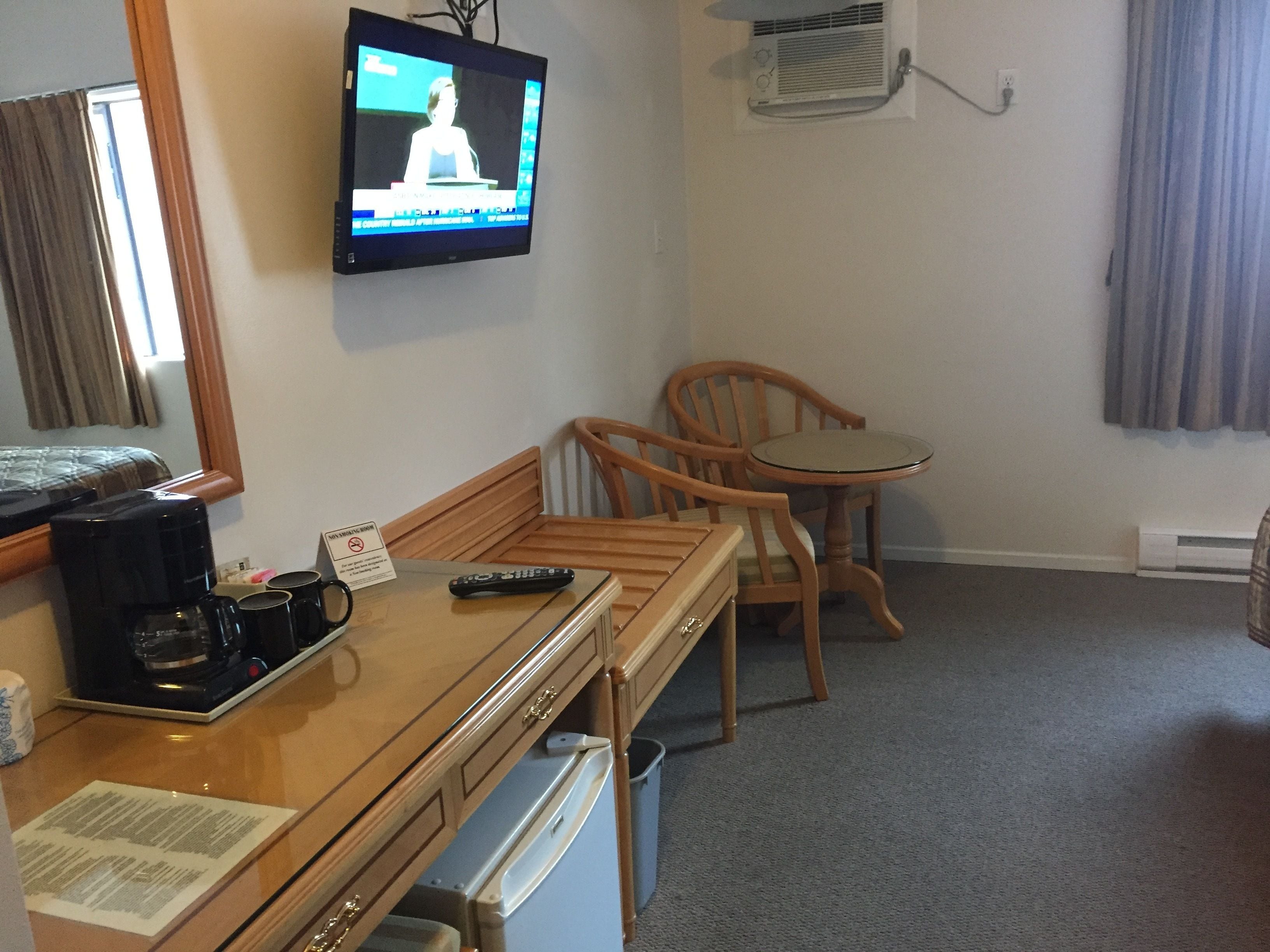 A hotel room with a bed, a desk with a coffee maker, a television, a chair, and a small table.